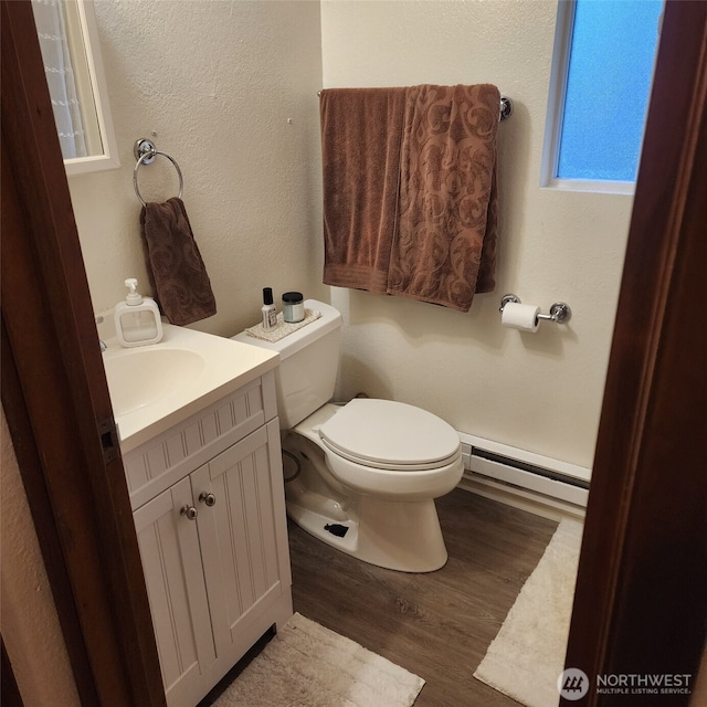 half bath with vanity, a baseboard radiator, wood finished floors, and toilet