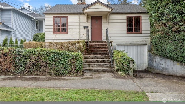 bungalow-style home featuring entry steps, a chimney, and roof with shingles