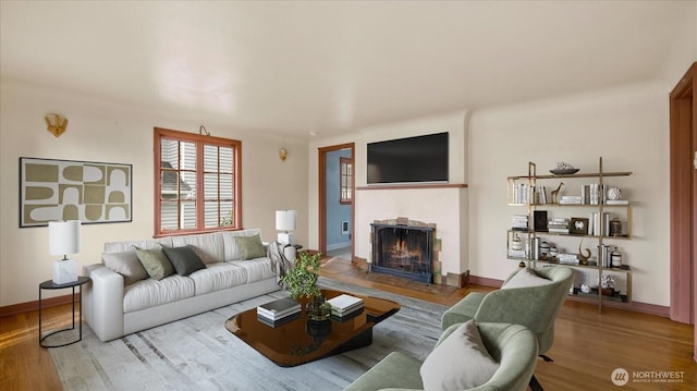 living room featuring wood finished floors, baseboards, and a warm lit fireplace