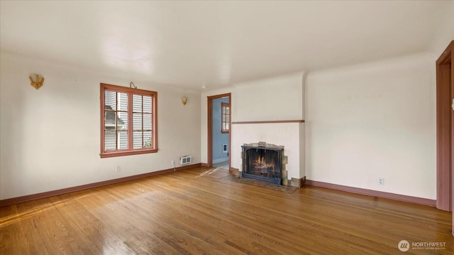 unfurnished living room with a fireplace with flush hearth, baseboards, visible vents, and wood finished floors