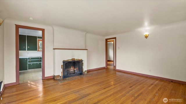 unfurnished living room featuring a fireplace with flush hearth, baseboards, and wood finished floors