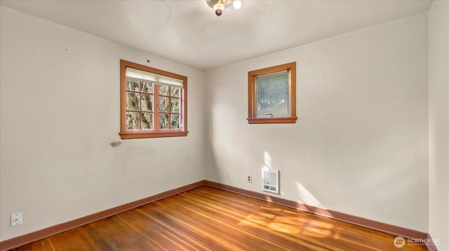 empty room with heating unit, wood finished floors, and baseboards