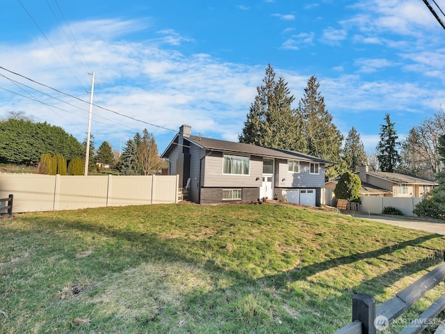 split foyer home with concrete driveway, a chimney, fence, a front yard, and brick siding