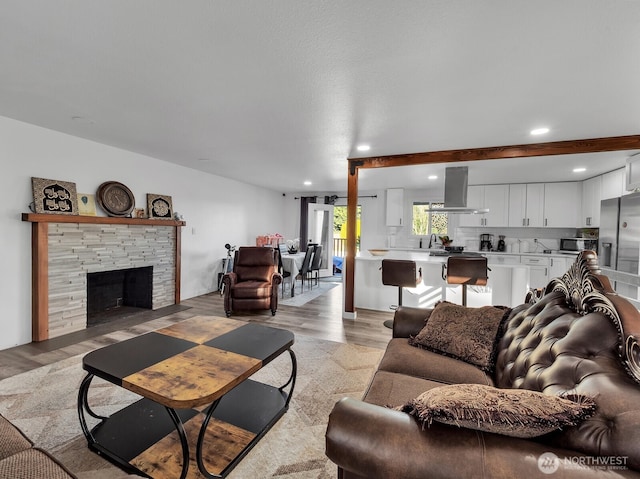 living area with light wood finished floors, a stone fireplace, and recessed lighting