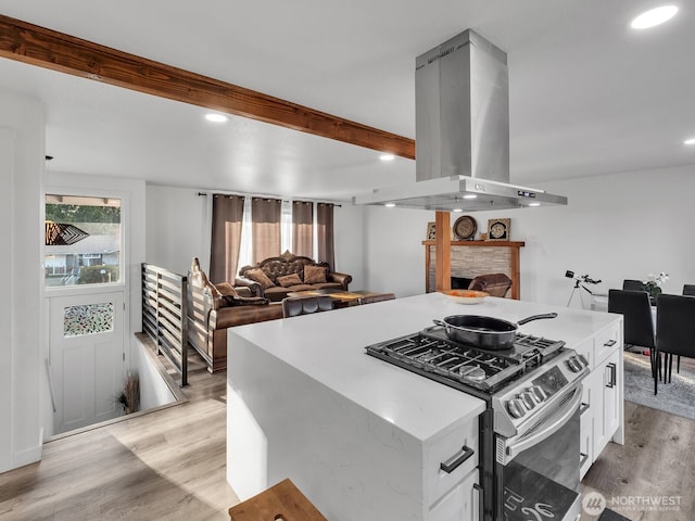 kitchen with island range hood, gas range, beamed ceiling, a stone fireplace, and light wood-type flooring