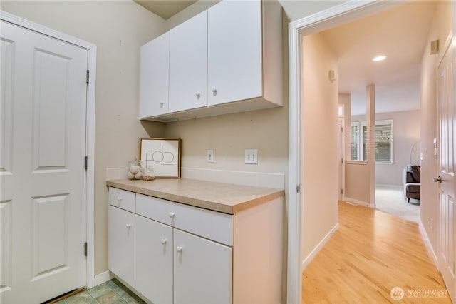 kitchen with light wood finished floors, baseboards, light countertops, recessed lighting, and white cabinetry