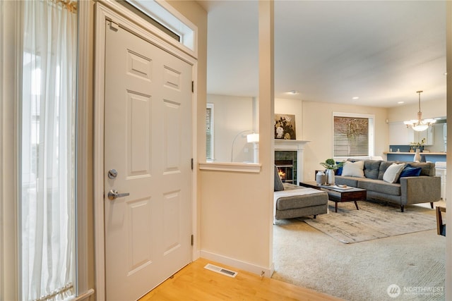 foyer with visible vents, light wood-style flooring, a tiled fireplace, an inviting chandelier, and baseboards