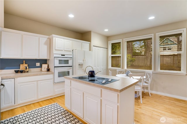 kitchen featuring light wood finished floors, white cabinets, white appliances, and a center island