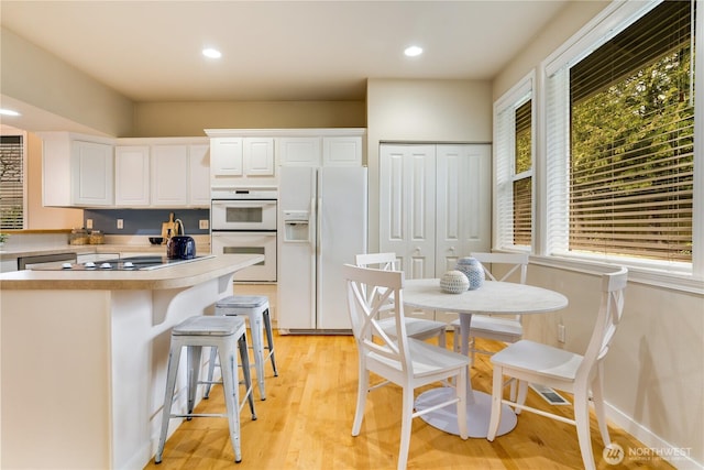 kitchen with light wood finished floors, a breakfast bar area, light countertops, white cabinets, and white appliances