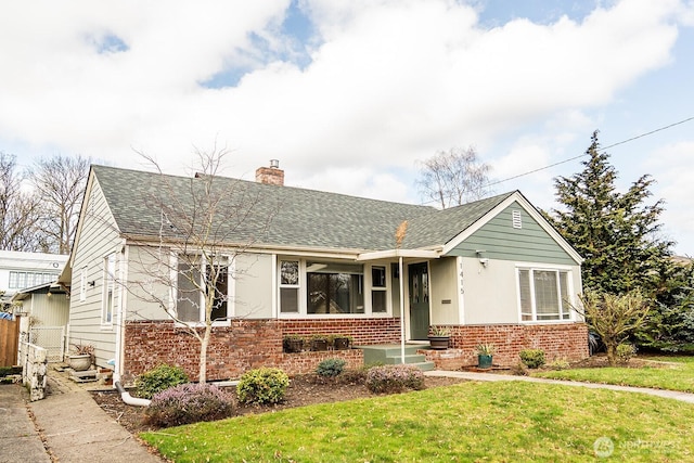 single story home with brick siding, fence, roof with shingles, a front lawn, and a chimney