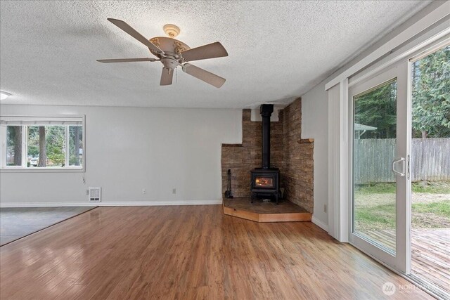 unfurnished living room with a textured ceiling, wood finished floors, and a wood stove