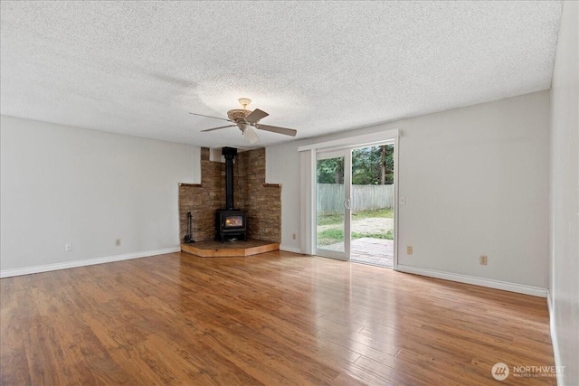 unfurnished living room featuring baseboards, a ceiling fan, wood finished floors, a wood stove, and a textured ceiling