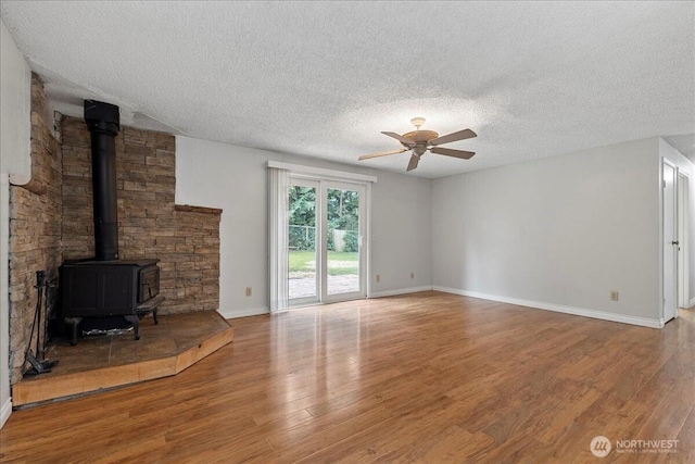 unfurnished living room featuring baseboards, ceiling fan, wood finished floors, a wood stove, and a textured ceiling