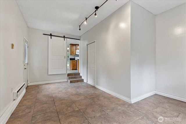 spare room with a baseboard heating unit, a textured ceiling, baseboards, and a barn door