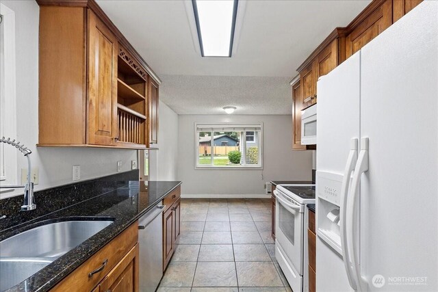 kitchen with brown cabinetry, white appliances, a sink, and a textured ceiling