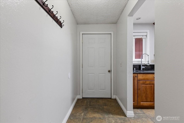 entryway with a textured ceiling, stone finish floor, a sink, and baseboards