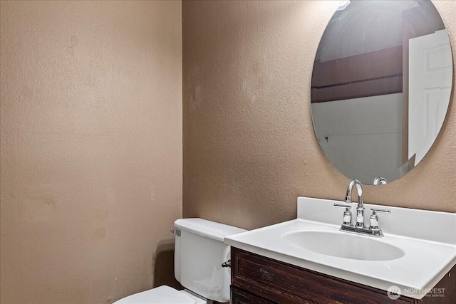 half bathroom with a textured wall, vanity, and toilet