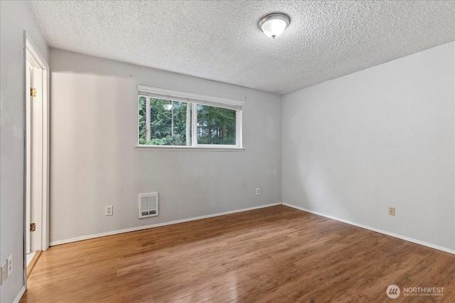 empty room featuring baseboards, a textured ceiling, visible vents, and wood finished floors