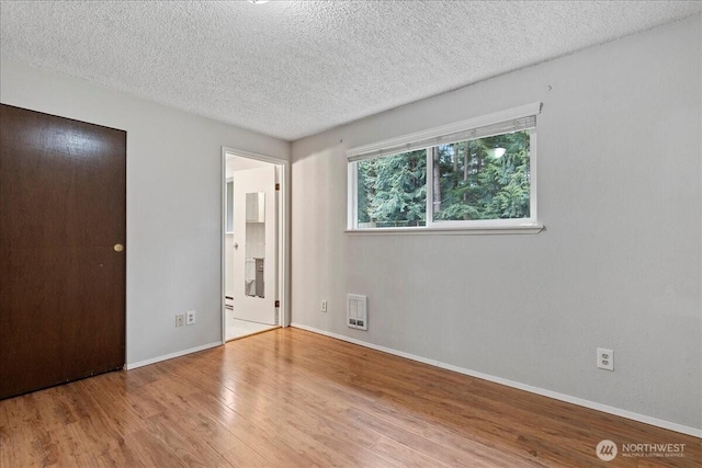 unfurnished bedroom with a textured ceiling, wood finished floors, visible vents, and baseboards