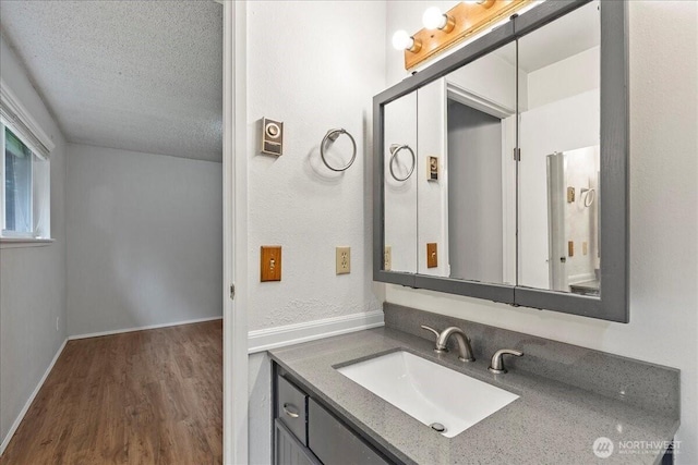 bathroom with a textured ceiling, wood finished floors, vanity, and baseboards