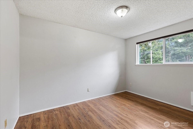 empty room with a textured ceiling, wood finished floors, and baseboards