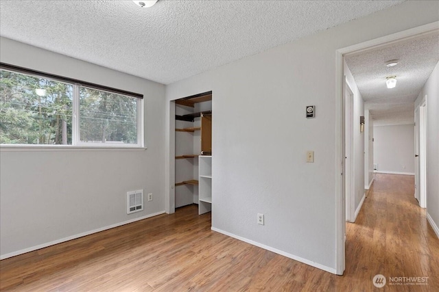 unfurnished bedroom with a textured ceiling, wood finished floors, visible vents, baseboards, and a closet