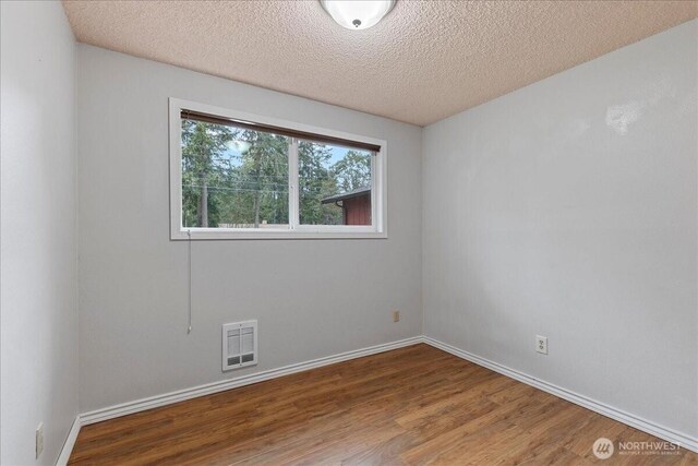 unfurnished room featuring baseboards, a textured ceiling, visible vents, and wood finished floors