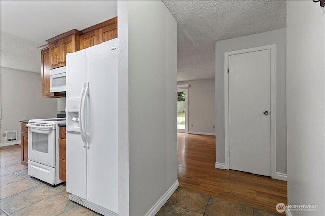 kitchen featuring a textured ceiling, white appliances, visible vents, and baseboards