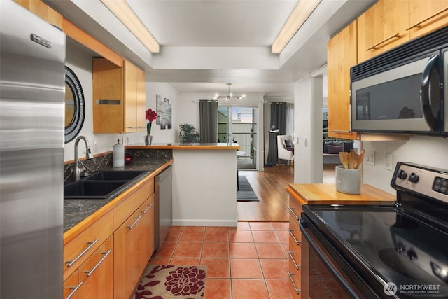 kitchen with a sink, a tray ceiling, appliances with stainless steel finishes, a peninsula, and tile patterned flooring