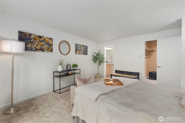 bedroom featuring a walk in closet, light colored carpet, baseboards, and connected bathroom