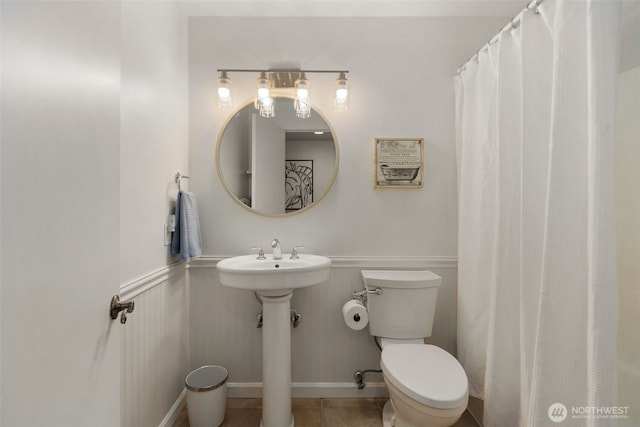 bathroom featuring tile patterned floors, a wainscoted wall, toilet, a sink, and a shower with shower curtain