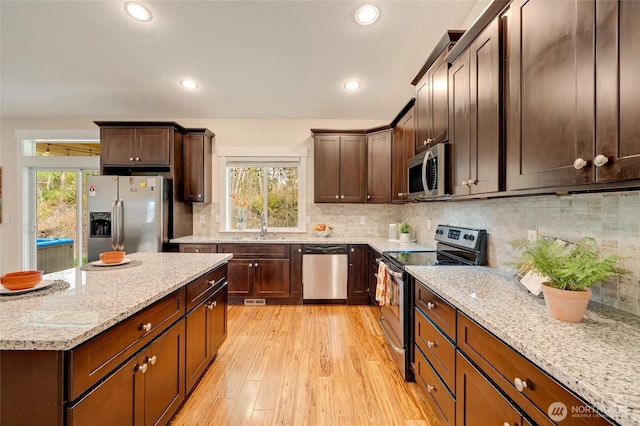 kitchen featuring stainless steel appliances, light wood-style floors, plenty of natural light, and light stone countertops