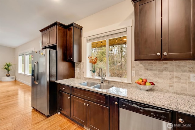 kitchen featuring stainless steel appliances, light wood-type flooring, a sink, and light stone countertops