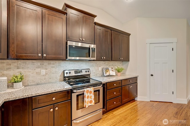 kitchen with tasteful backsplash, lofted ceiling, appliances with stainless steel finishes, light stone counters, and light wood-style floors