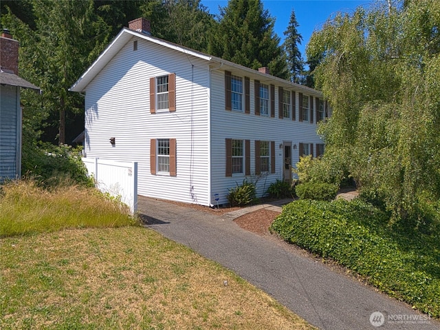 view of front of home featuring aphalt driveway, a chimney, and a front lawn