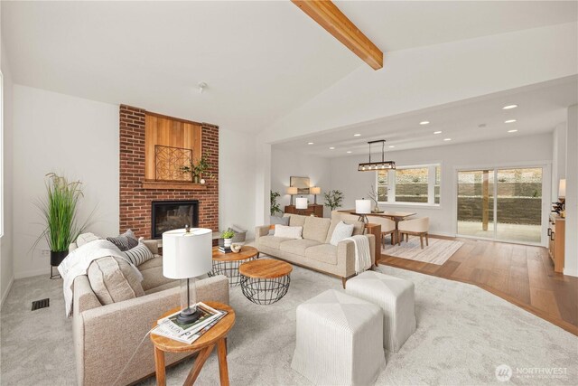 living area featuring visible vents, lofted ceiling with beams, light wood-type flooring, a brick fireplace, and recessed lighting