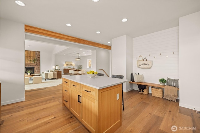 kitchen with light wood-style flooring, a breakfast bar area, a center island, light countertops, and a brick fireplace