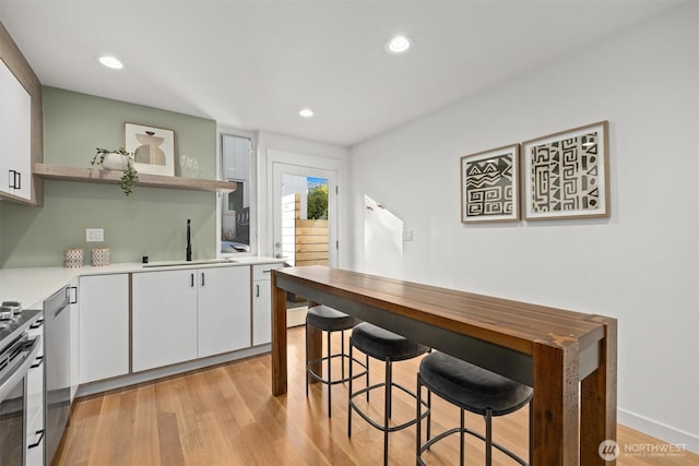 kitchen featuring light wood finished floors, open shelves, light countertops, white cabinets, and a sink