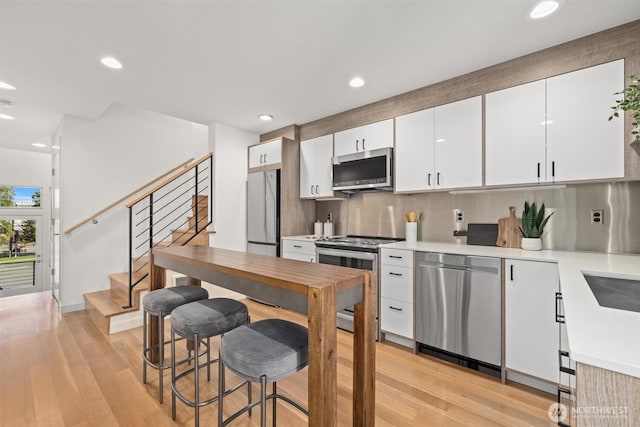 kitchen with stainless steel appliances, white cabinets, light countertops, and light wood-style flooring