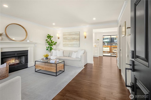 living room with dark wood finished floors, recessed lighting, ornamental molding, a warm lit fireplace, and baseboards