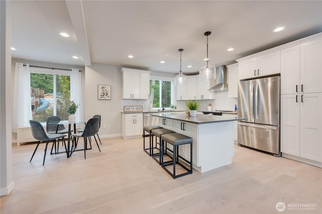 kitchen featuring a breakfast bar, a center island, stainless steel appliances, wall chimney exhaust hood, and white cabinets