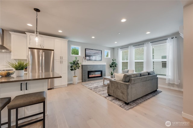 living room featuring a tiled fireplace, recessed lighting, light wood-type flooring, and baseboards