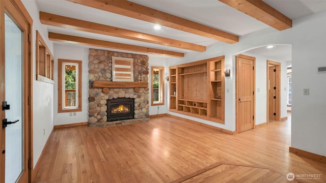 unfurnished living room with light wood finished floors, beamed ceiling, a fireplace, and baseboards