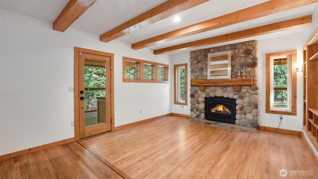 unfurnished living room featuring beam ceiling, baseboards, wood finished floors, and a stone fireplace