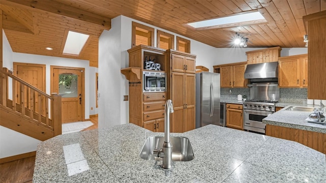 kitchen with wooden ceiling, lofted ceiling with skylight, appliances with stainless steel finishes, range hood, and backsplash