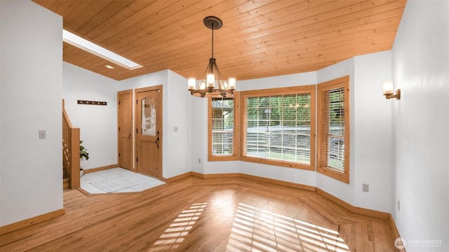 foyer entrance featuring baseboards, vaulted ceiling with skylight, wood finished floors, and a notable chandelier