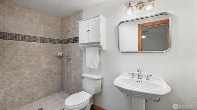 bathroom with tiled shower, a sink, and toilet