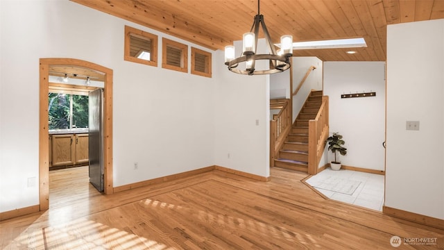 unfurnished dining area with light wood-style flooring, a notable chandelier, wood ceiling, baseboards, and stairs