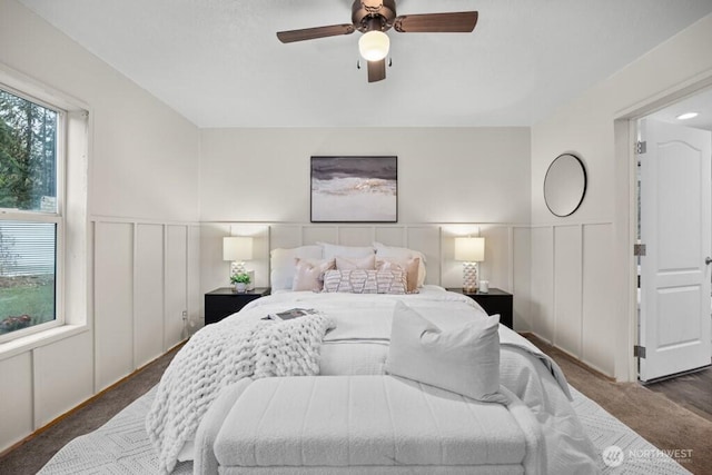 bedroom featuring ceiling fan, carpet, a decorative wall, and a wainscoted wall