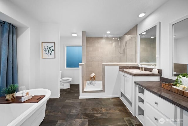 bathroom with a walk in shower, a freestanding tub, and vanity